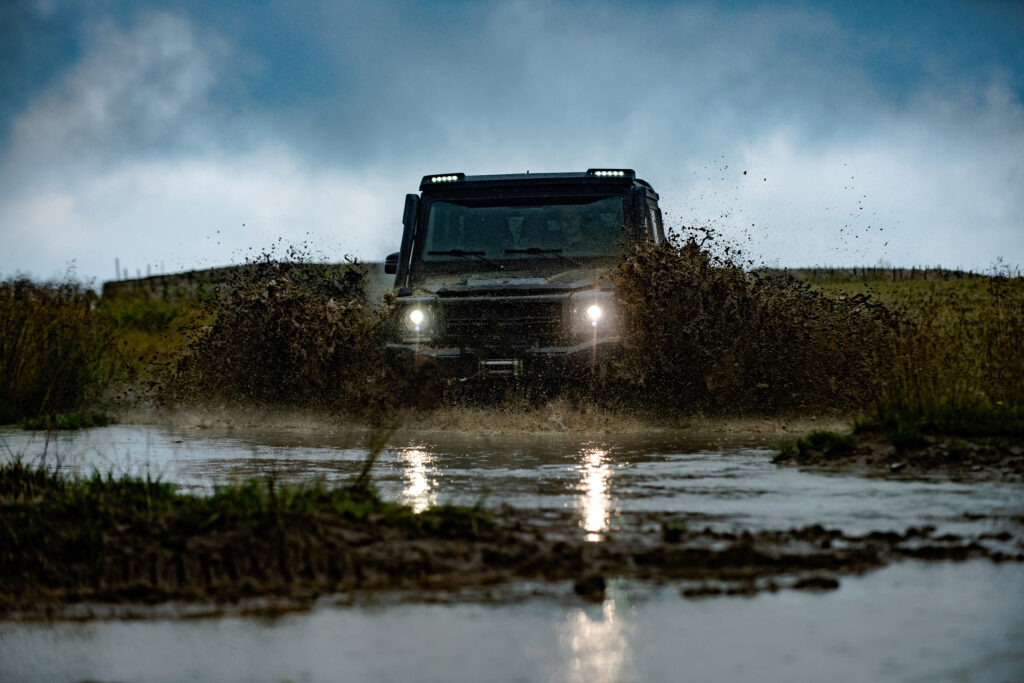 Wheel close up in a countryside landscape with a muddy road. Water splash in off road racing. Off road vehicle coming out of a mud hole hazard