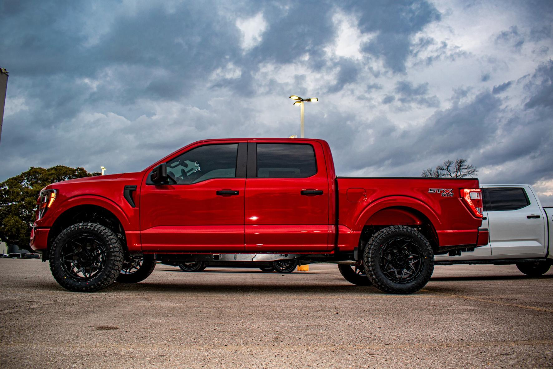 Red off-road truck with custom black wheels parked under cloudy sky, showcasing rugged design and paint protection importance for off-road vehicles.